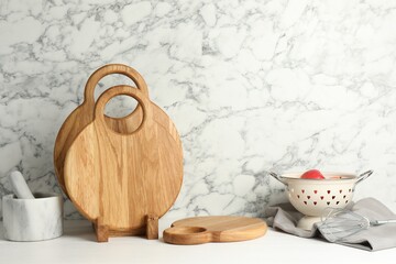 Wooden cutting boards, mortar with pestle and colander on white table near marble wall