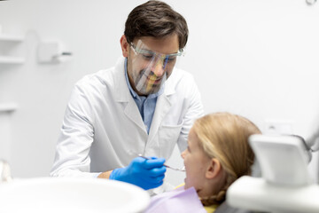 Kid girl taking care of her teeth while male dentist orthodontist in mask examining whitening dental cavity. Stomatology medicine concept