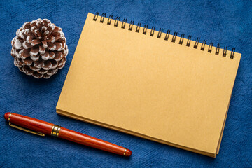 blank spiral notebook with a decorative frosty pine cone and luxury pen on art paper