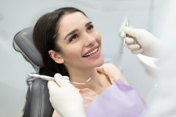 Smiling happy female client in dental chair with doctor looking at her perfect teeth with instruments
