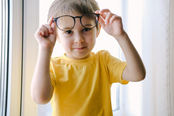Little toddler boy wearing yellow T-shirt is taking off the glasses