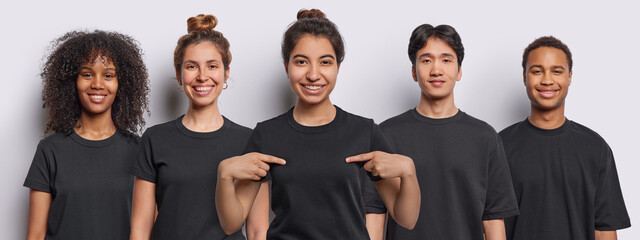 Horizontal shot of cheerful mixed race women and men dressed in black t shirts Latin woman points...
