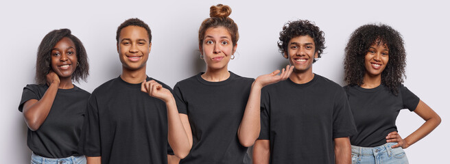 Positive mixed race millennial people smile toothily one expresses hesitation and spreads palms sideways dressed in casual black t shirts look directly at camera isolated over white background. - obrazy, fototapety, plakaty