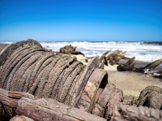 Skeleton Coast National Park, Namibia - August 21, 2022: A close-up of a shipwreck's weathered rope and timber against the backdrop of rough sea waves.