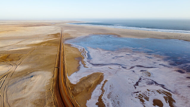 Skeleton Coast National Park, Namibia - August 21, 2022: Aerial view of a vast salt flat adjacent to a solitary road, with the ocean in the distance under a clear sky