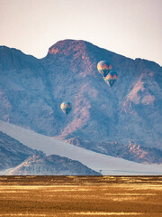 Sesriem, Namibia - August 24, 2022: The image captures the serene beauty of hot air balloons floating at dawn against a rugged mountain backdrop.