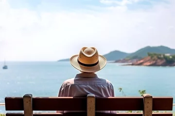 Foto op Canvas Elderly man sits on bench by the ocean in summer day. Senior man in hat. Back view. © Iryna