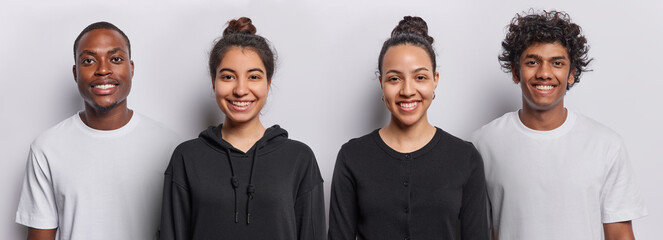 Two positive diverse young women smile gladfully stand between two men being all in good mood stand in black and white t shirts pose indoor. Smiling female models and guys express happy emotions