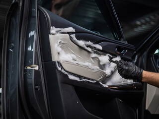 A man cleans the interior of a car with foam and a brush. Clean the door trim.