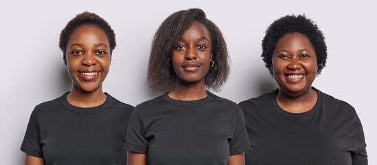Portrait of three African American sisters look directly at camera have satisfied expressions...