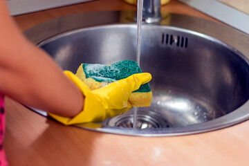 Close Up Of Female Hands In Rubber Protective Yellow Gloves Cleaning The Kitchen Sink With Rag....