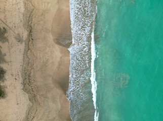 beach water from above (drone shot looking down at turquoise blue green waves, surf, sand, palm tree shadow) coastline on luquillo beach, puerto rico (playa la pared beach) daytime dusk sunset