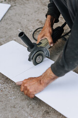 A man, a worker in an outdoor workshop, cuts off a plastic material for insulation with a grinder, an electric cutter.