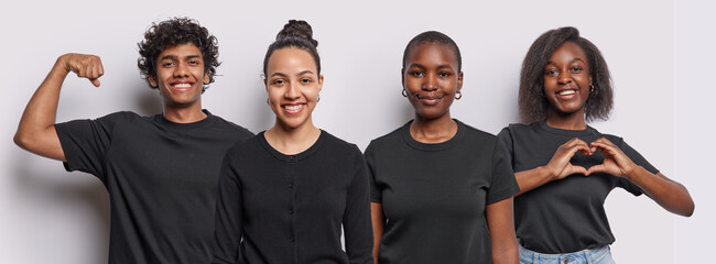 Horizontal shot of three diverse young women and one Hindu man smile pleasantly show heart gesture and raise arm demonstrates biceps wear same black t shirts isolated over white studio background. - Powered by Adobe