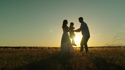 Happy family leisure on field with fun and joy feeling togetherness at sunset. Father spins daughter and gives kid to dancing mother hugs. Family dreamy flight of childhood at evening darkness