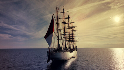 Aerial drone photo of beautiful three mast barque or barc type classic sailing wooden boat with huge waving flag anchored in Mediterranean deep blue Aegean sea at sunset with golden colours - obrazy, fototapety, plakaty