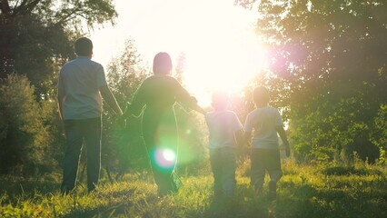 Happy children and joyful parents walk joining hands across meadow on family weekend. Small...