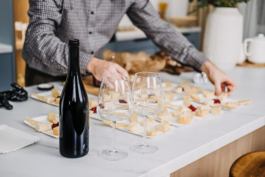 Catering Professional Arranging Cheese Plates for Service. Professional catering expert in black gloves places slices of cheese on individual plates for event, with backdrop of wine and fresh bread.