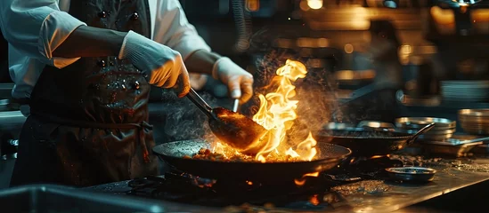 Foto op Plexiglas Professional chef wearing gloves and apron cooking stir fry flambe holding a pan with open fire in a dark restaurant kitchen. Creative Banner. Copyspace image © HN Works