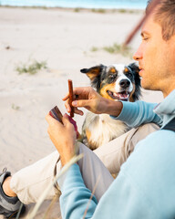 Man playing with his dog, Australian Shepherd on a beach. young caucasian male on beach while...