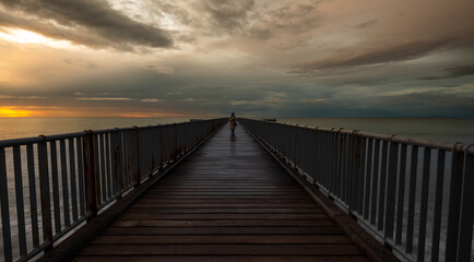 Fototapeta na wymiar Person walking alone on a pier enjoying dramatic sunset at the sea. Exploring nature
