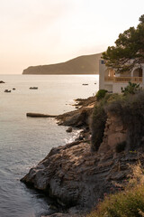 Rocky coastline with a house on the rocks in a sunset that creates a warm atmosphere in the town of...