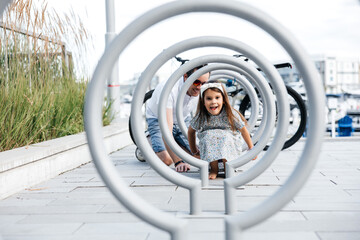 A dad with his little daughter is having fun and sticking out his tongue while walking on the...