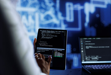 Admin updates neural networks made up of interconnected nodes, writing intricate binary code scripts on tablet and laptop, close up. Data center expert uses programming to upgrade AI simulation model