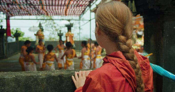 Balinese Kecak Dance ceremony in ancient Hindu temple in Indonesia. Indonesian girls dressed in traditional costumes dance in Bali Nusa Penida Island. Female tourist watching the process.