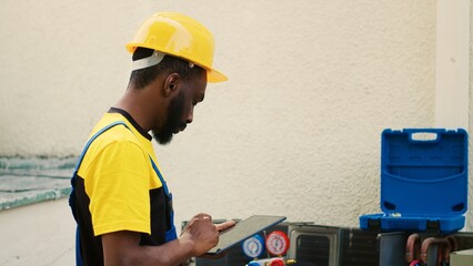 Smiling technician happy with refrigerant levels in external air conditioner while using manifold...