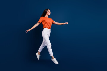 Fototapeta na wymiar Full length photo of funky pretty woman dressed orange t-shirt jumping high walking empty space isolated dark blue color background