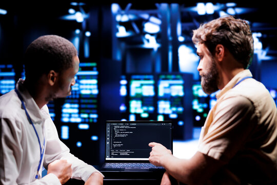 IT developers coworkers writing script code in server room on laptop terminal. Teamworking programmers doing maintenance work in technologically advanced data center updating racks software
