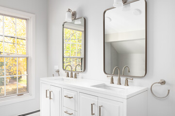A bathroom detail with a white cabinet, bronze faucets and mirrors, and colorful trees out the...