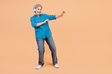 Fototapeta na wymiar Full size photo of positive retired woman dressed stylish shirt in headphones dancing near empty space isolated on pastel color background