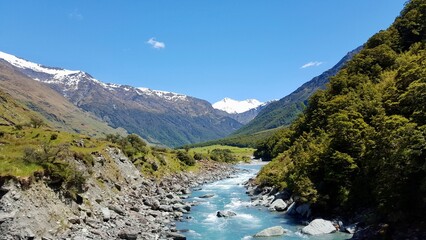 Fototapeta na wymiar New zealand river blue water with green rocks and mountains with snow blue sky