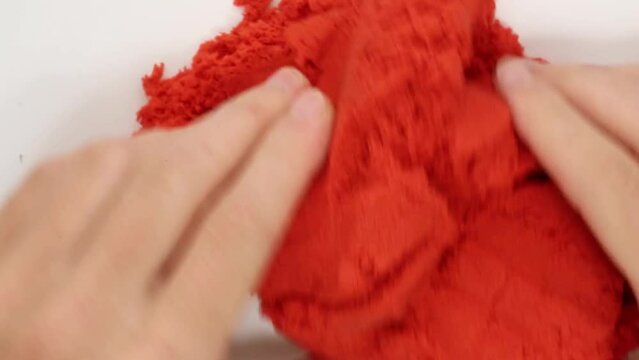 Human hands are pressing crumbly, malleable kinetic red sand. Asmr. A relaxing