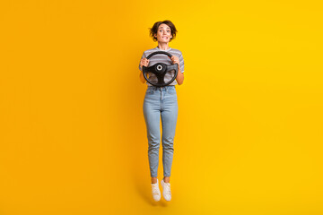 Fototapeta na wymiar Full size portrait of nervous pretty girl jumping biting lips hands hold wheel isolated on yellow color background