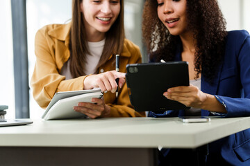 Caucasian and an African American university woman working together on a project, using a laptop and talking on a phone.