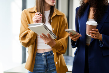 Obraz premium Caucasian and an African American university woman engaged in a conversation, holding a notebook and a coffee cup.