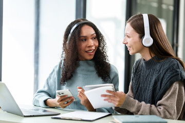 Caucasian and an African American university woman working together on a project, discussing and taking notes.