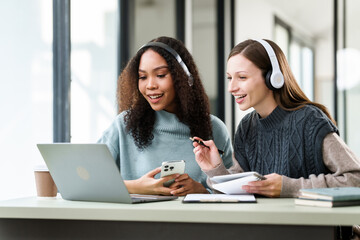 Caucasian and an African American university woman working together on a project, discussing and taking notes.
