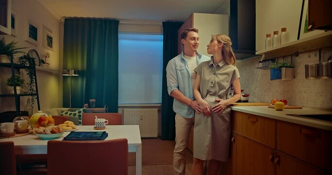 Happy man embracing his pregnant wife in kitchen of modern apartment, 4K, Prores