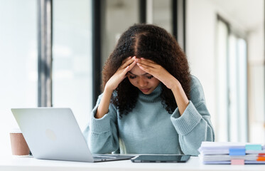 African American university student looking worried or stressed while working on her MBA project on a laptop at her desk.