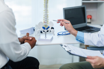 Close up male doctor and patient people in a medical office, spine model, possibly discussing...