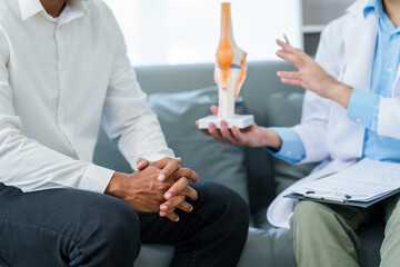 male patient and male doctor discussing a model of a knee joint, likely focusing on condition of knee arthritis during a medical consultation. - obrazy, fototapety, plakaty