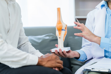 male patient and male doctor discussing a model of a knee joint, likely focusing on condition of...