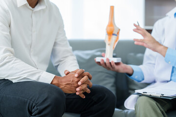 male patient and male doctor discussing a model of a knee joint, likely focusing on condition of knee arthritis during a medical consultation.