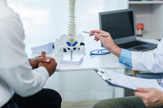 Close up male doctor and patient people in a medical office, spine model, possibly discussing spinal condition or syndrome with the patient.