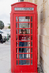 Obraz premium Classic red telephone booth. A girl inside a telephone booth.