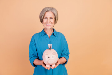 Photo of good mood woman with bob hairdo dressed blue shirt hold money piggy box with banknote isolated on pastel color background